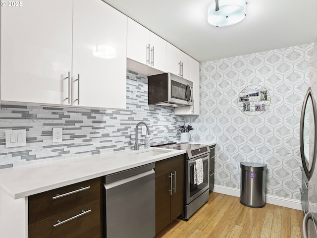 kitchen with white cabinets, stainless steel appliances, dark brown cabinets, light countertops, and light wood-style floors