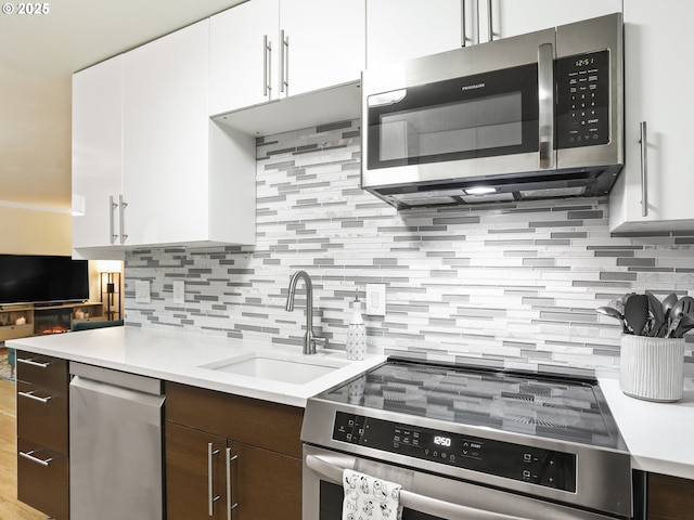 kitchen with white cabinets, stainless steel appliances, a sink, and light countertops