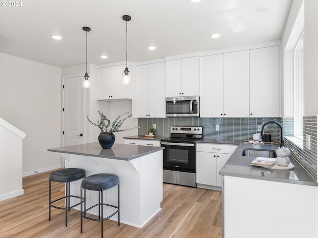 kitchen featuring white cabinets, appliances with stainless steel finishes, a center island, decorative light fixtures, and sink