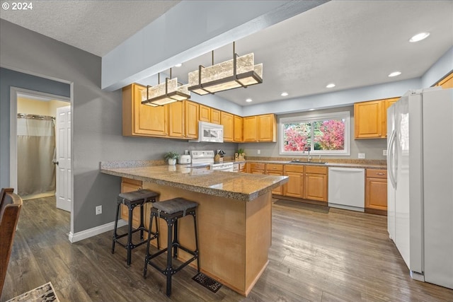 kitchen featuring white appliances, sink, kitchen peninsula, a breakfast bar area, and dark hardwood / wood-style floors