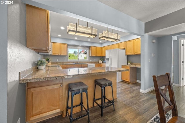 kitchen with a breakfast bar area, dark wood-type flooring, kitchen peninsula, sink, and white appliances