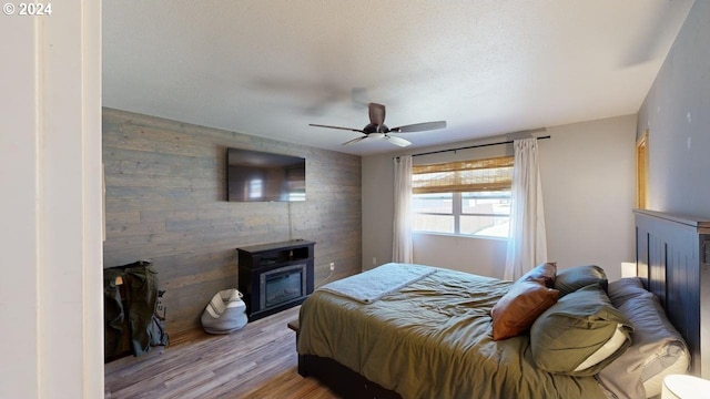 bedroom featuring a textured ceiling, a wood stove, ceiling fan, and light wood-type flooring