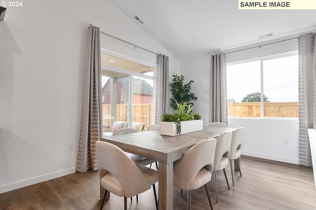 dining space featuring wood-type flooring, vaulted ceiling, and a wealth of natural light