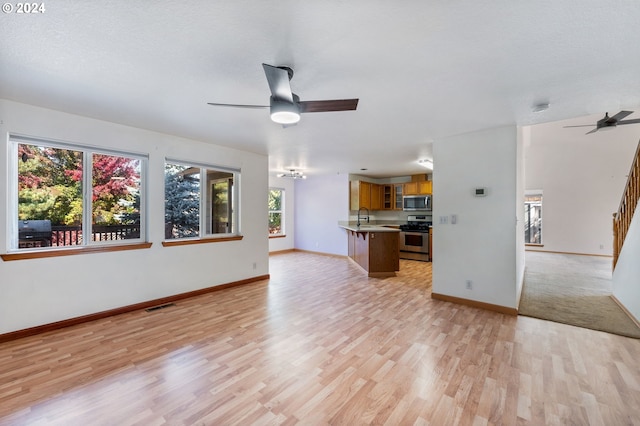 unfurnished living room featuring ceiling fan, sink, a textured ceiling, and light wood-type flooring