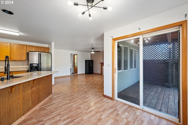 kitchen with stainless steel fridge, ceiling fan with notable chandelier, a textured ceiling, sink, and light hardwood / wood-style floors