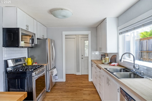 4524 NE 41st Ave, Portland, OR 97211 - kitchen with stainless steel appliances, a sink, light wood finished floors, white cabinetry, and decorative backsplash