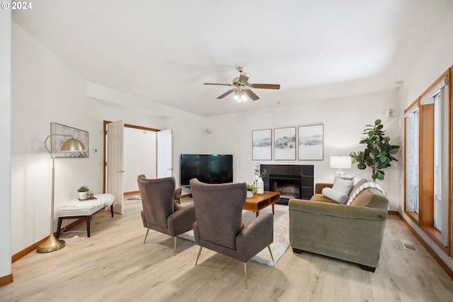 living room featuring a tiled fireplace, ceiling fan, and light hardwood / wood-style flooring