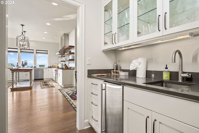 bar featuring dark hardwood / wood-style flooring, hanging light fixtures, wall chimney exhaust hood, stainless steel dishwasher, and white cabinets