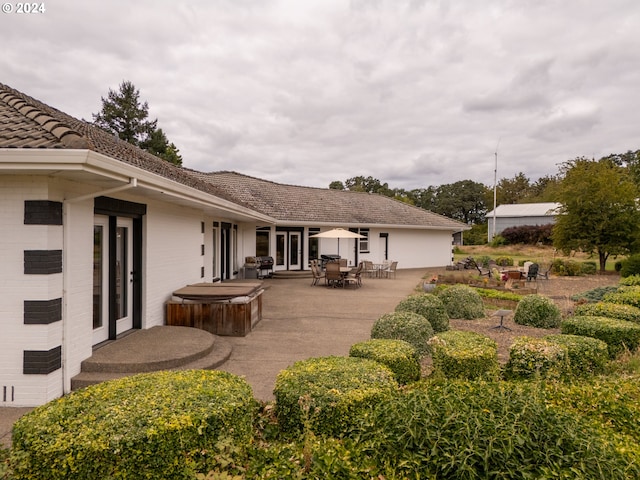 rear view of property with a hot tub and a patio