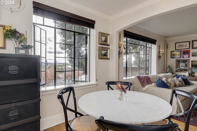 dining space with arched walkways, crown molding, plenty of natural light, and light wood-style floors