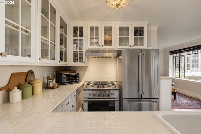 kitchen featuring tile counters, backsplash, white cabinets, high quality appliances, and under cabinet range hood