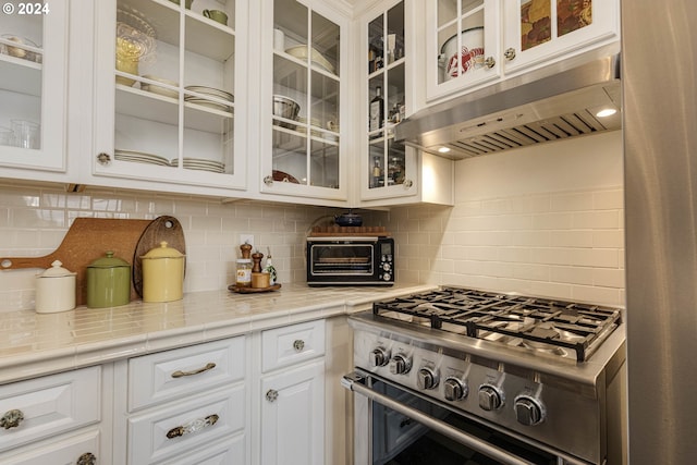 kitchen with a toaster, backsplash, white cabinetry, high end stove, and under cabinet range hood