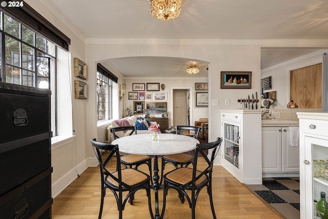 dining area with arched walkways, light wood finished floors, baseboards, and crown molding