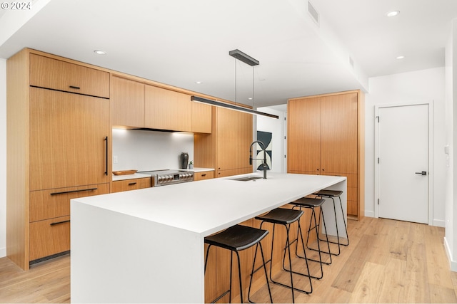 kitchen with hanging light fixtures, a kitchen island with sink, light countertops, and a sink