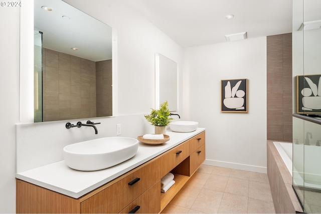 full bath with a relaxing tiled tub, double vanity, a sink, and tile patterned floors