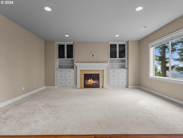 unfurnished living room with a textured ceiling, light colored carpet, and a tile fireplace