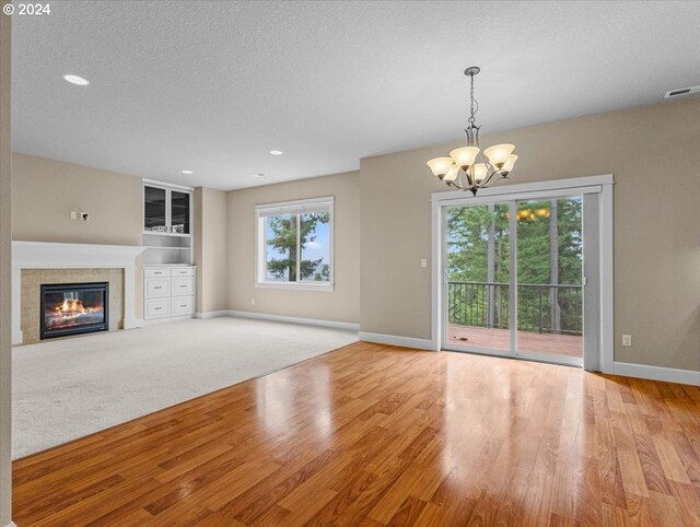 unfurnished living room featuring a textured ceiling, a notable chandelier, a tiled fireplace, and light wood-type flooring