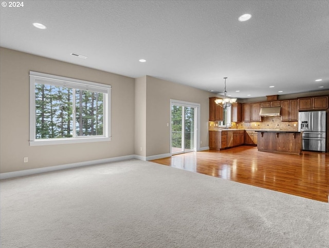 unfurnished living room featuring light wood-type flooring, sink, a notable chandelier, and a textured ceiling