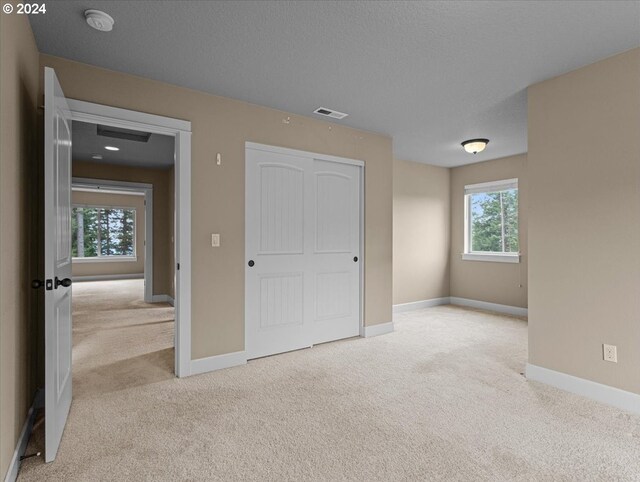 unfurnished bedroom featuring a closet, light carpet, and a textured ceiling