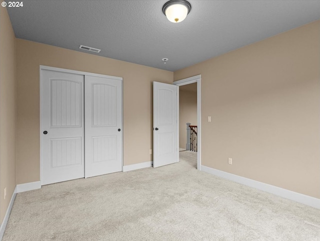 unfurnished bedroom featuring light carpet, a textured ceiling, and a closet