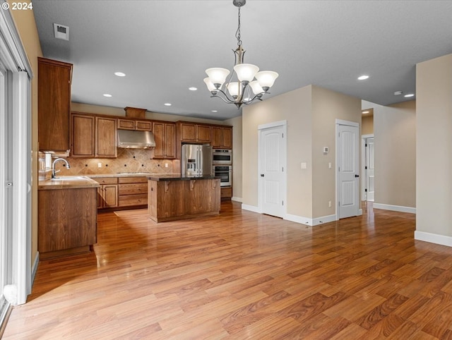 kitchen with pendant lighting, a notable chandelier, a kitchen island, appliances with stainless steel finishes, and light hardwood / wood-style floors