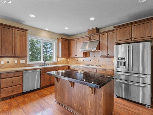 kitchen featuring appliances with stainless steel finishes, tasteful backsplash, light hardwood / wood-style floors, a breakfast bar, and sink