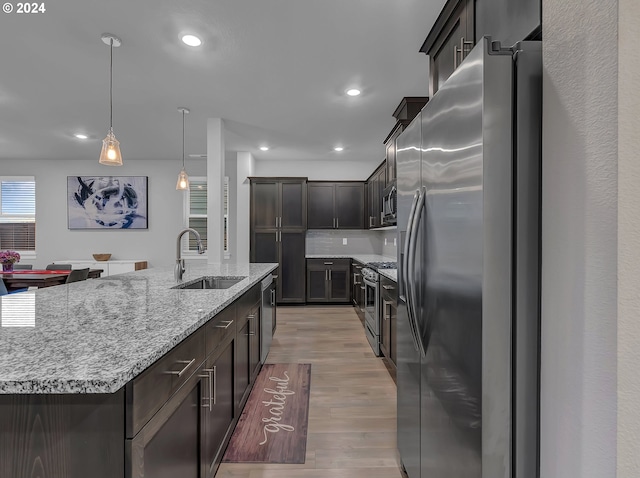 kitchen with a large island with sink, hanging light fixtures, sink, light hardwood / wood-style floors, and stainless steel appliances