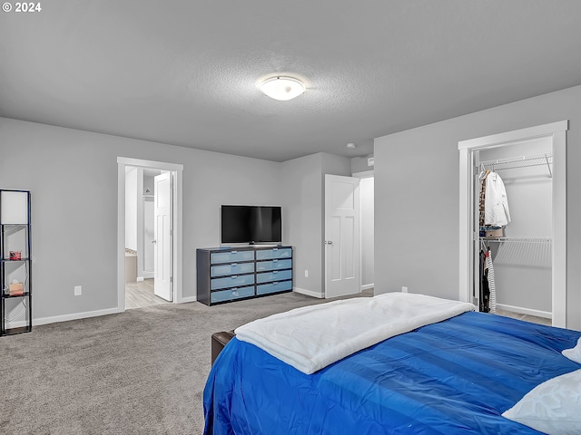 carpeted bedroom with connected bathroom, a walk in closet, a closet, and a textured ceiling