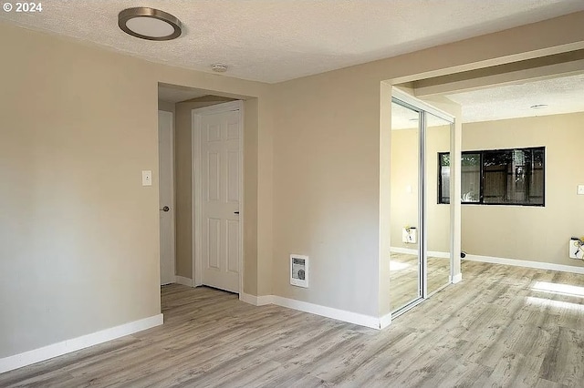 hallway with light hardwood / wood-style flooring, a textured ceiling, and heating unit