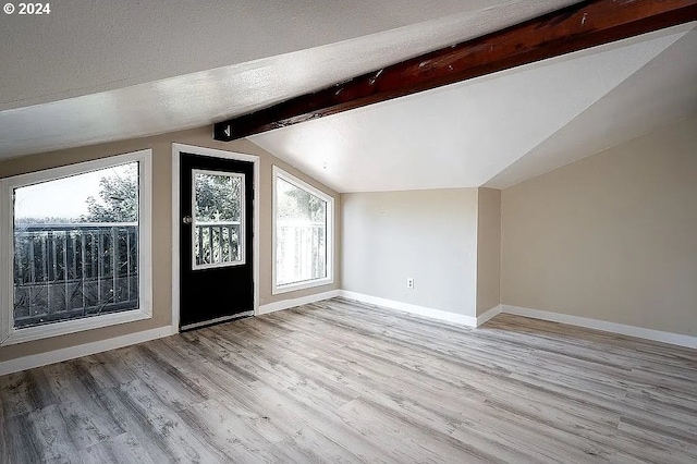 additional living space with light hardwood / wood-style floors, a healthy amount of sunlight, lofted ceiling with beams, and a textured ceiling