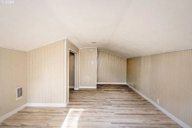 bonus room featuring lofted ceiling, light wood-type flooring, and wood walls