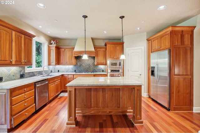 kitchen with hanging light fixtures, a kitchen island, stainless steel appliances, light wood-type flooring, and sink