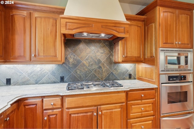 kitchen with light stone counters, custom exhaust hood, stainless steel appliances, and tasteful backsplash