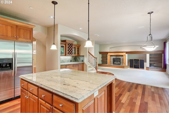 kitchen featuring a tile fireplace, stainless steel refrigerator with ice dispenser, light wood-type flooring, and hanging light fixtures