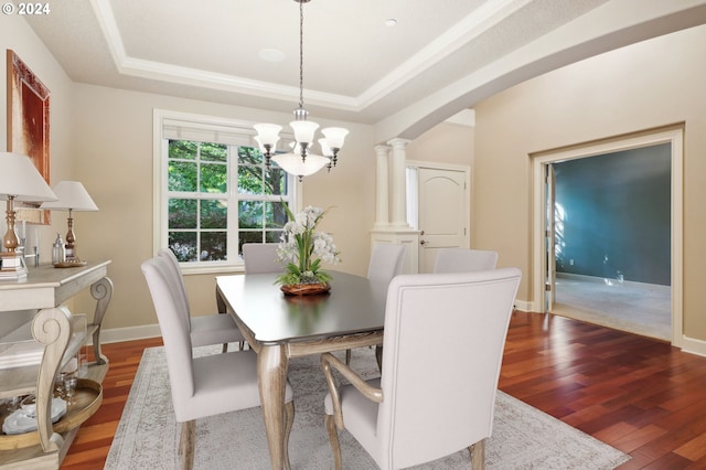 dining room featuring wood-type flooring, a notable chandelier, a tray ceiling, and decorative columns