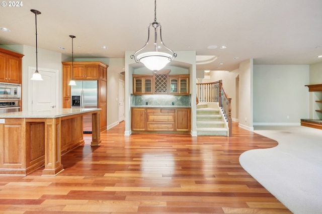 kitchen with pendant lighting, light hardwood / wood-style floors, a center island, decorative backsplash, and appliances with stainless steel finishes