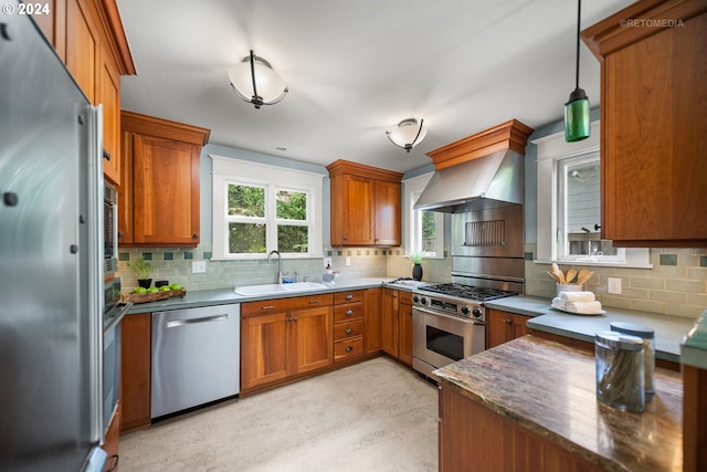 kitchen with wall chimney range hood, backsplash, sink, decorative light fixtures, and appliances with stainless steel finishes