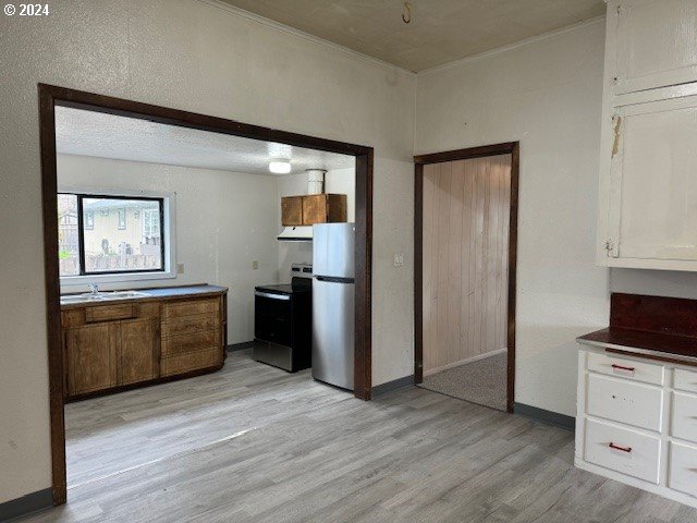 kitchen with appliances with stainless steel finishes, brown cabinets, light wood-type flooring, under cabinet range hood, and white cabinetry