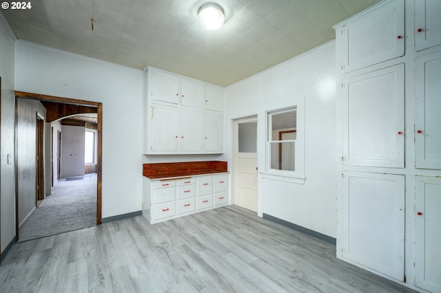 kitchen with baseboards, arched walkways, white cabinets, crown molding, and light wood-style floors