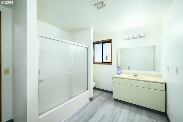 bathroom featuring toilet, bath / shower combo with glass door, wood finished floors, vanity, and visible vents