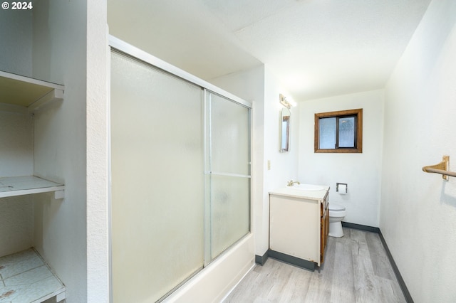 full bath with baseboards, bath / shower combo with glass door, toilet, wood finished floors, and vanity