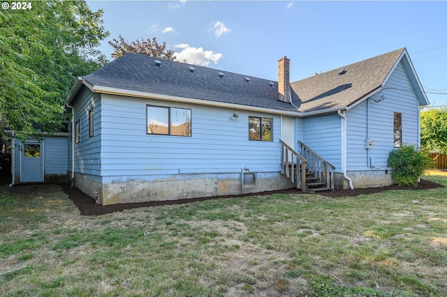 rear view of property with entry steps, a yard, a chimney, and roof with shingles