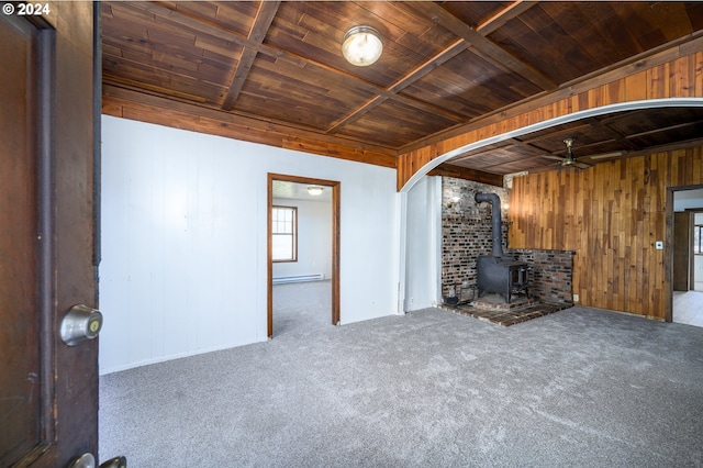 unfurnished living room with ceiling fan, carpet floors, a wood stove, and wooden ceiling