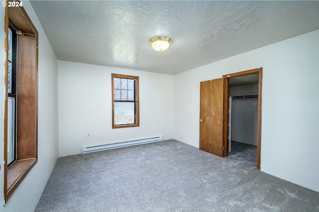 unfurnished bedroom with carpet, a walk in closet, a textured ceiling, and baseboard heating