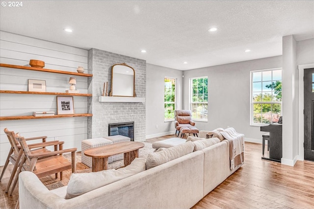 living room featuring a brick fireplace, plenty of natural light, a textured ceiling, and light hardwood / wood-style flooring