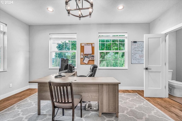 office space featuring a notable chandelier, light hardwood / wood-style floors, a textured ceiling, and a wealth of natural light