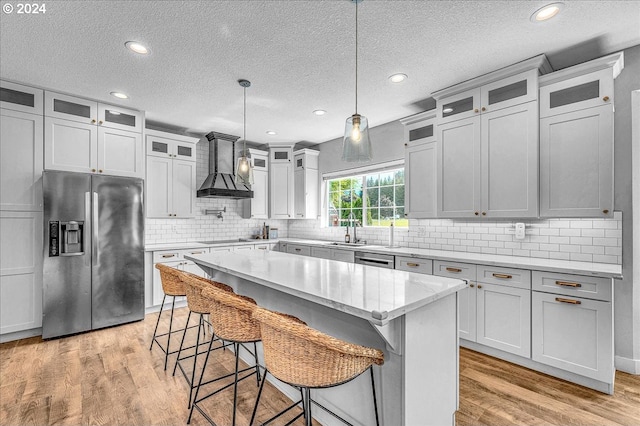 kitchen with appliances with stainless steel finishes, custom range hood, sink, decorative light fixtures, and a center island