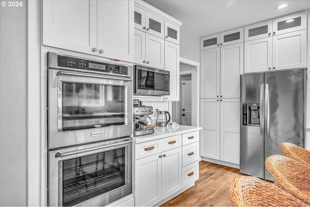 kitchen with light wood-type flooring, white cabinetry, a textured ceiling, and appliances with stainless steel finishes