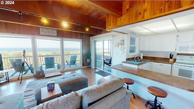 living room featuring beam ceiling, sink, rail lighting, wood walls, and light wood-type flooring