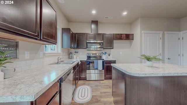 kitchen featuring light wood finished floors, stainless steel appliances, light countertops, a sink, and dark brown cabinets